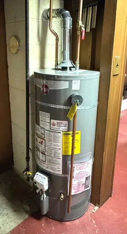 Water heater in a small utility closet with exposed pipes and a yellow gas line.