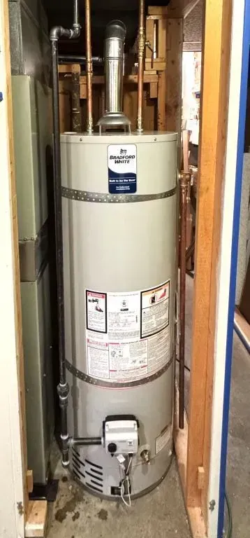 Water heater in a narrow utility closet with exposed pipes and valves