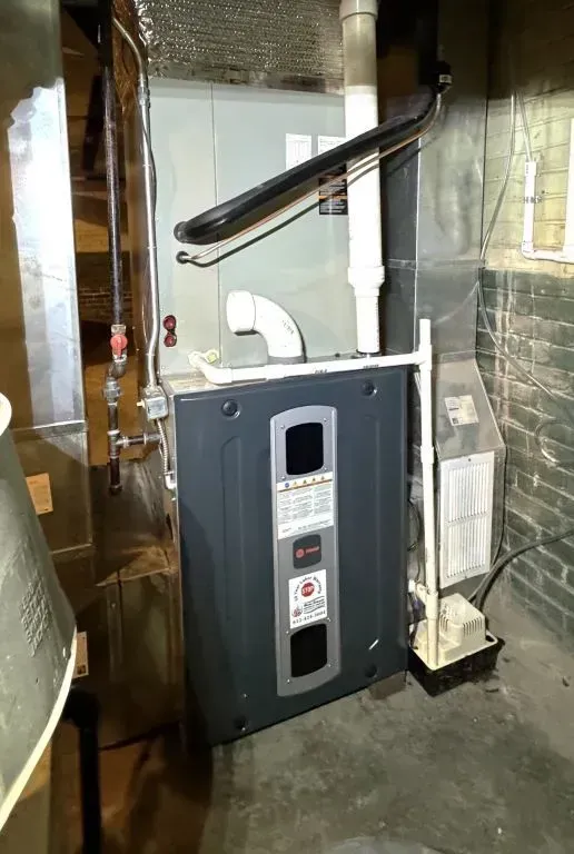Basement furnace and HVAC system with white vent pipes and ductwork in a utility room.