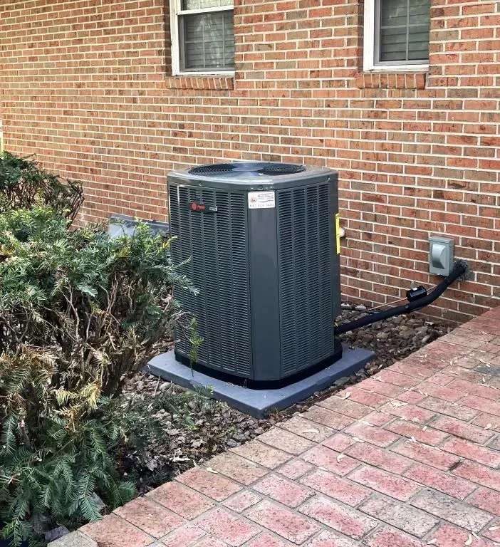 Outdoor air conditioning unit beside a brick house and walkway