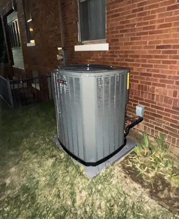 Outdoor air conditioner unit beside a brick house at night