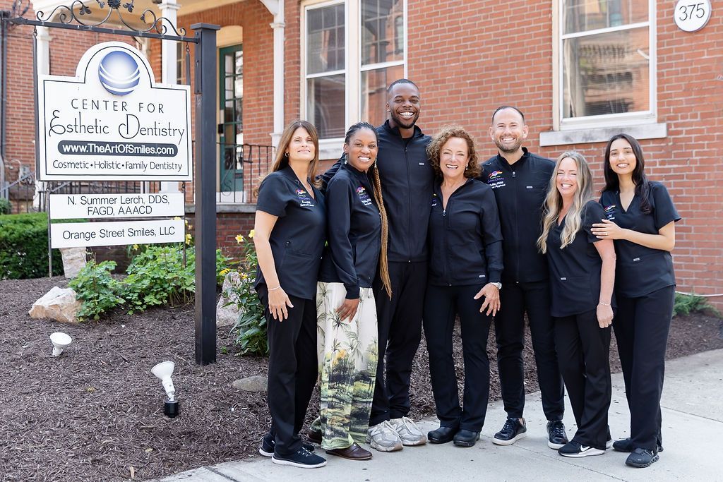 Six people in black outfits standing outside a brick building beside a sign.