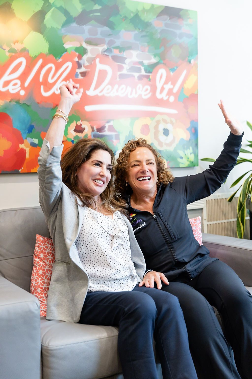 Two smiling people on a couch with arms raised in a colorful office lounge