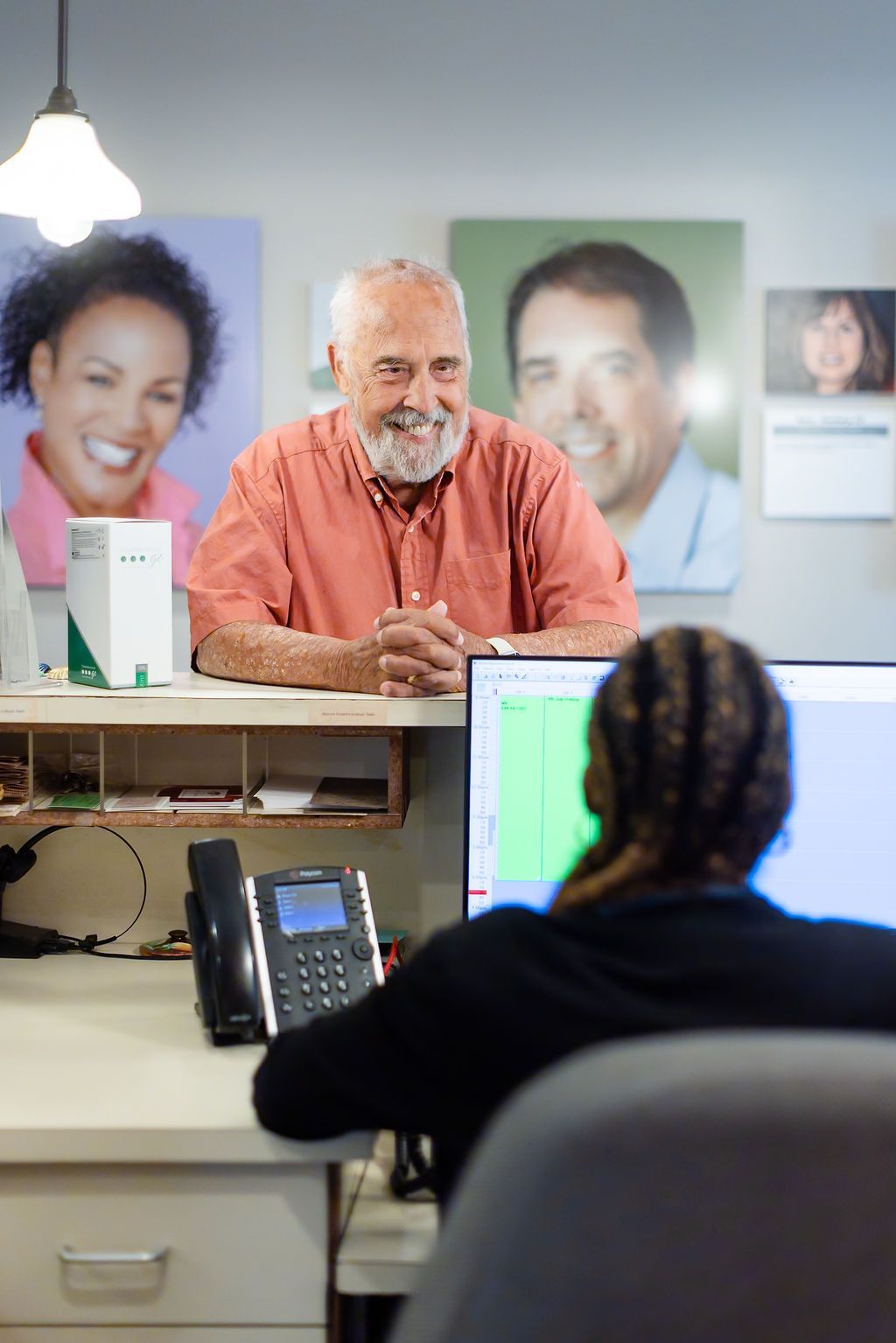 Man seated at a desk across from a receptionist in a bright office with portrait photos on the wall