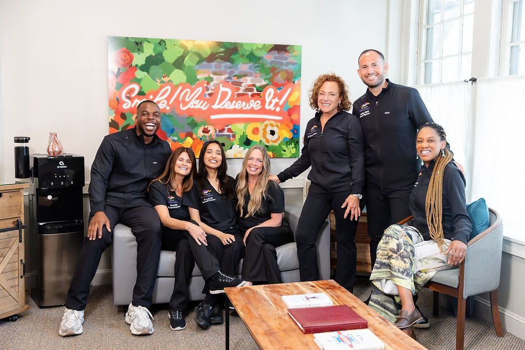 Six people posing on a couch and chairs in a bright room with a colorful mural behind them.