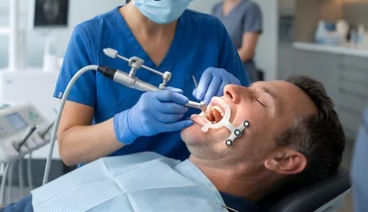 Dentist treating a patient in a clinic, using dental tools and a face mask.