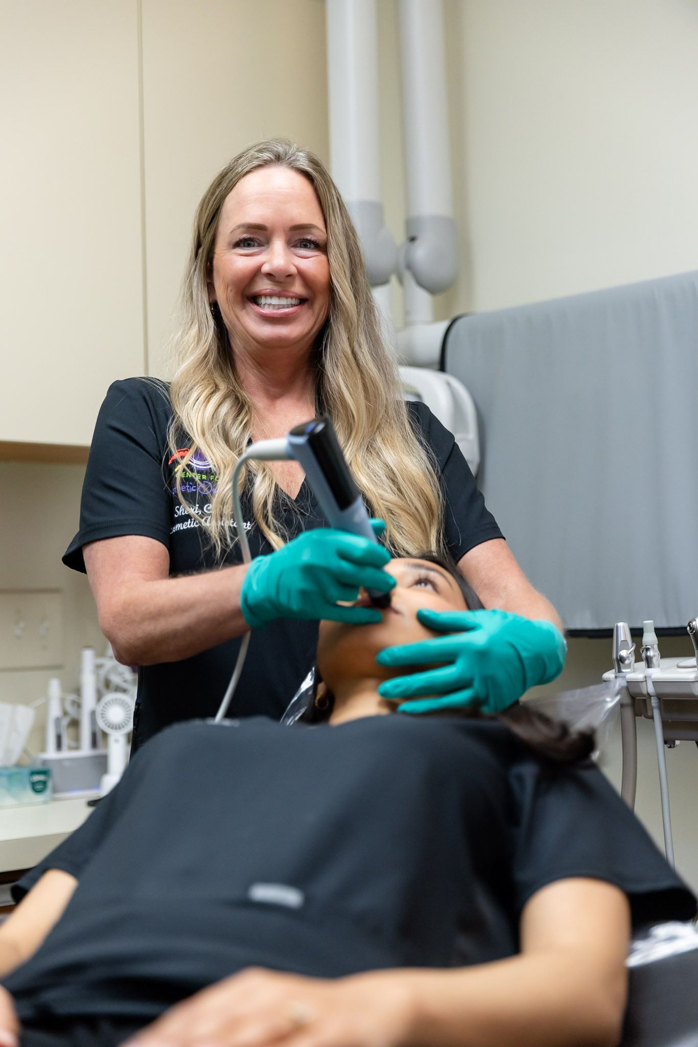Dentist smiling while examining a patient in a dental chair with teal gloves.