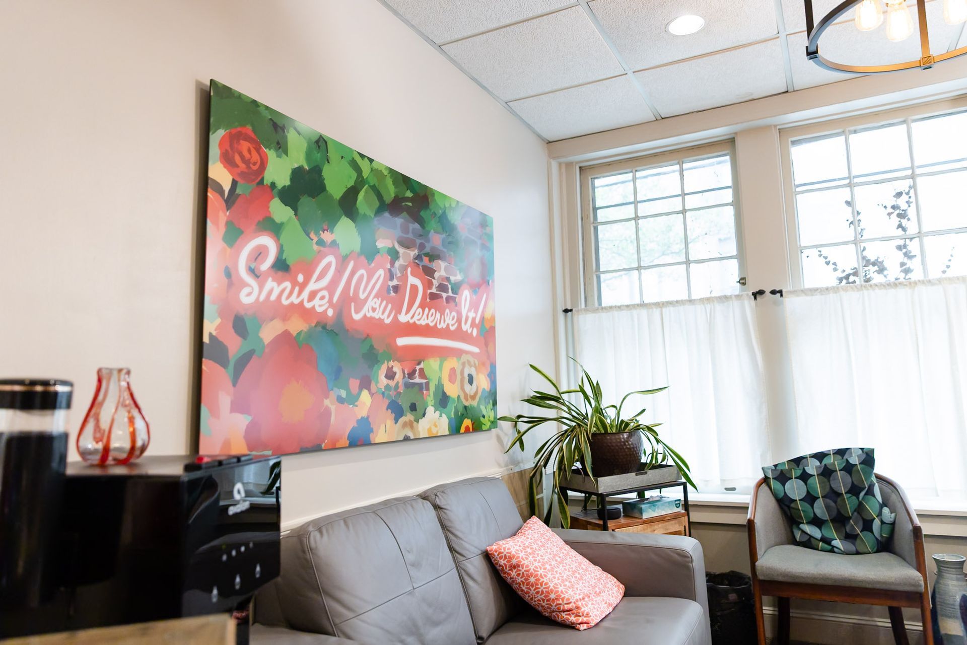 Bright living room with gray sofa, colorful wall art, chair, and large window with sheer curtains