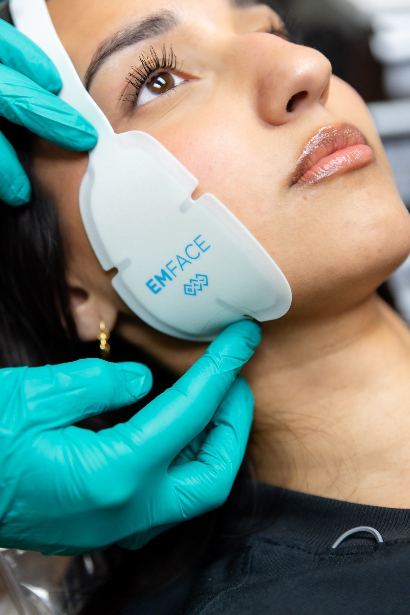 Gloved hands holding a facial treatment device against a woman’s cheek