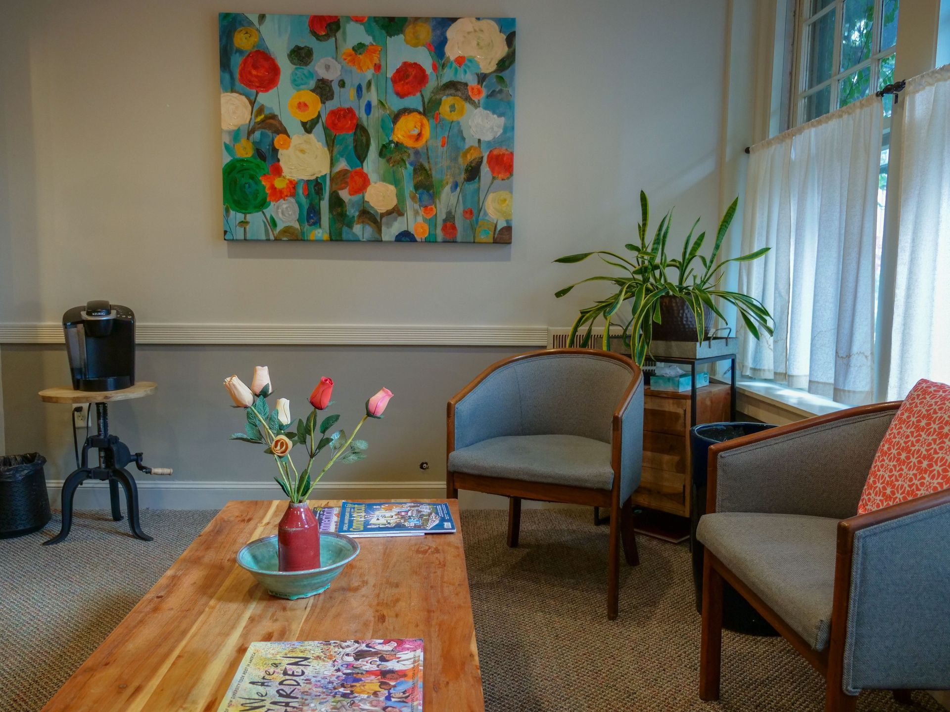 Cozy waiting room with chairs, coffee table, flowers, plants, and colorful wall art