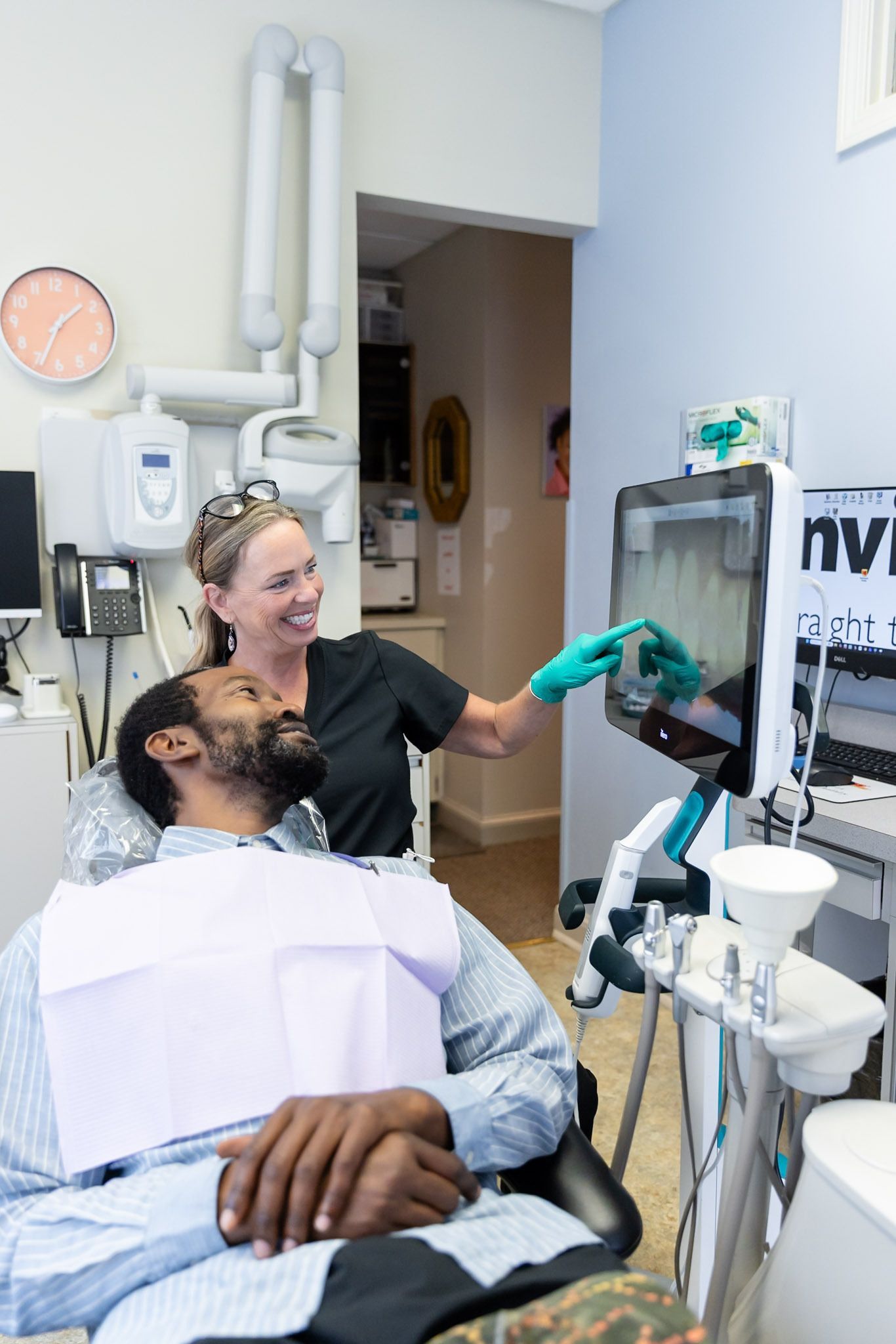 Patient and clinician in a dental exam room, with the clinician pointing at a monitor.