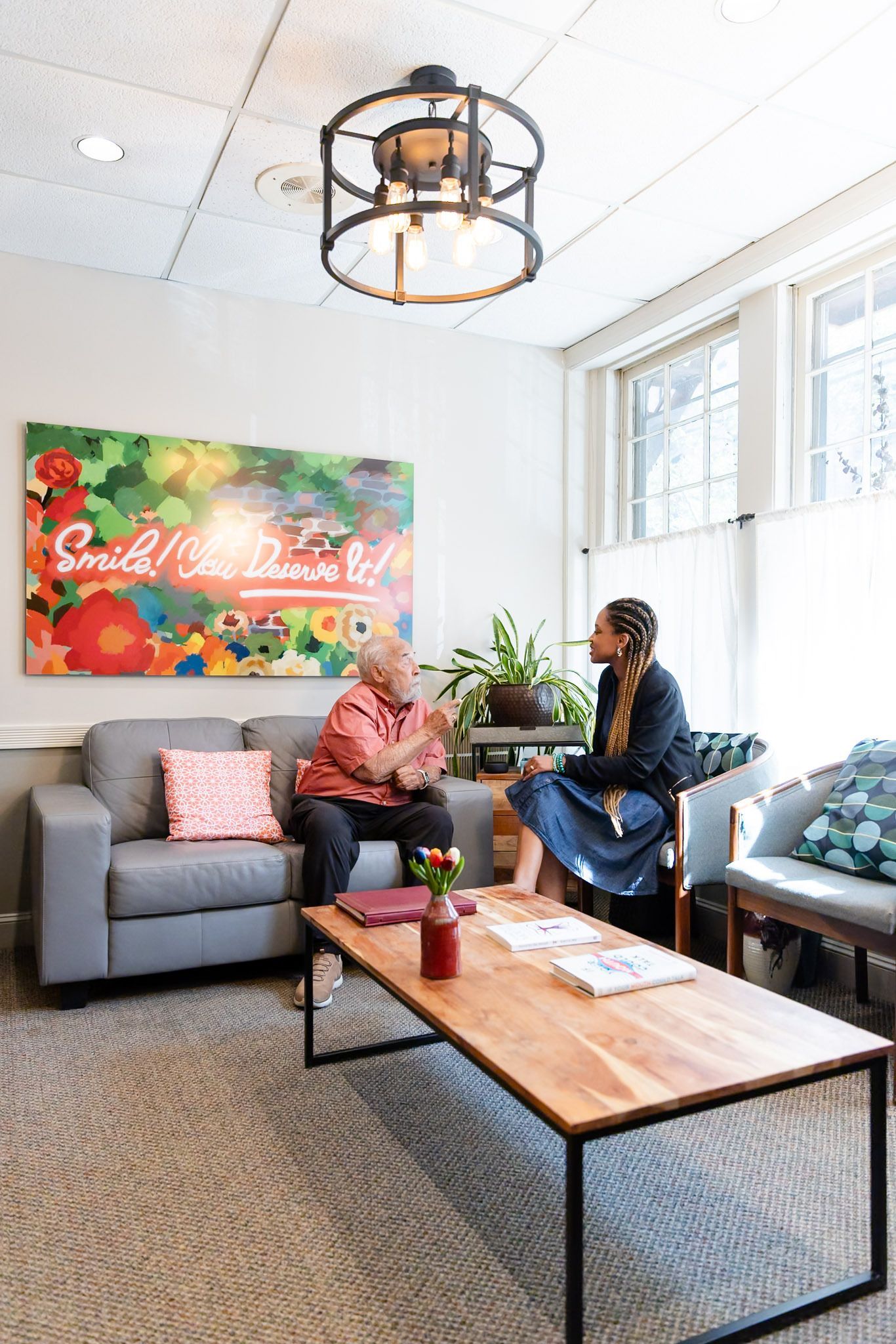 Two people sit chatting in a bright lobby with gray sofas