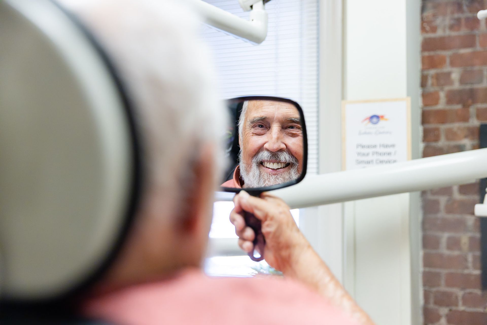 Person smiling in dental chair while looking in mirror at teeth aligned by braces