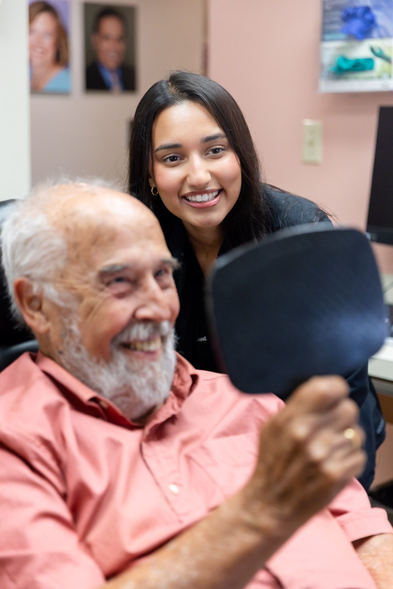 Smiling man holds a hand mirror while a woman stands behind him in a bright room