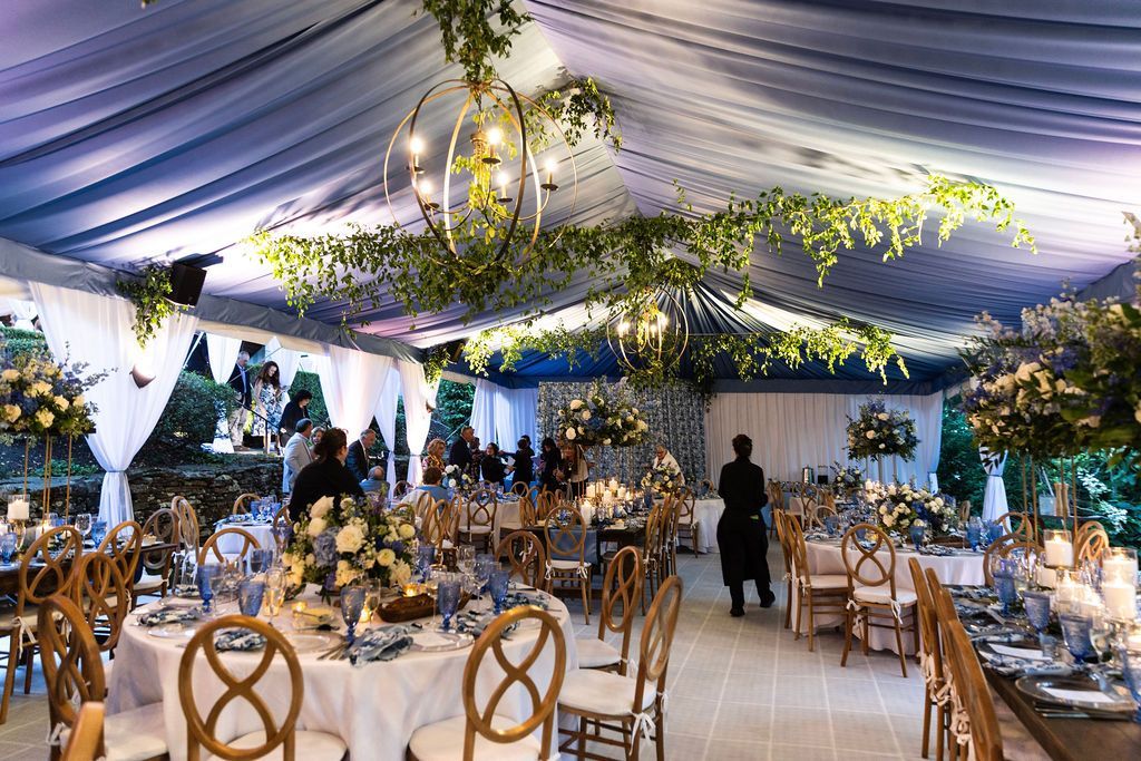 Elegant banquet hall with gold chairs, floral centerpieces, and a blue draped ceiling under warm lights