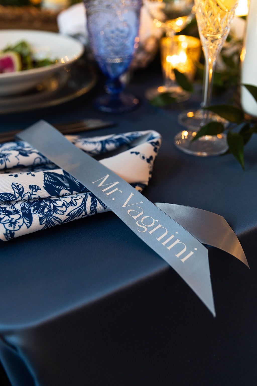 Blue-and-white napkin with ribbon place card on a dark table setting