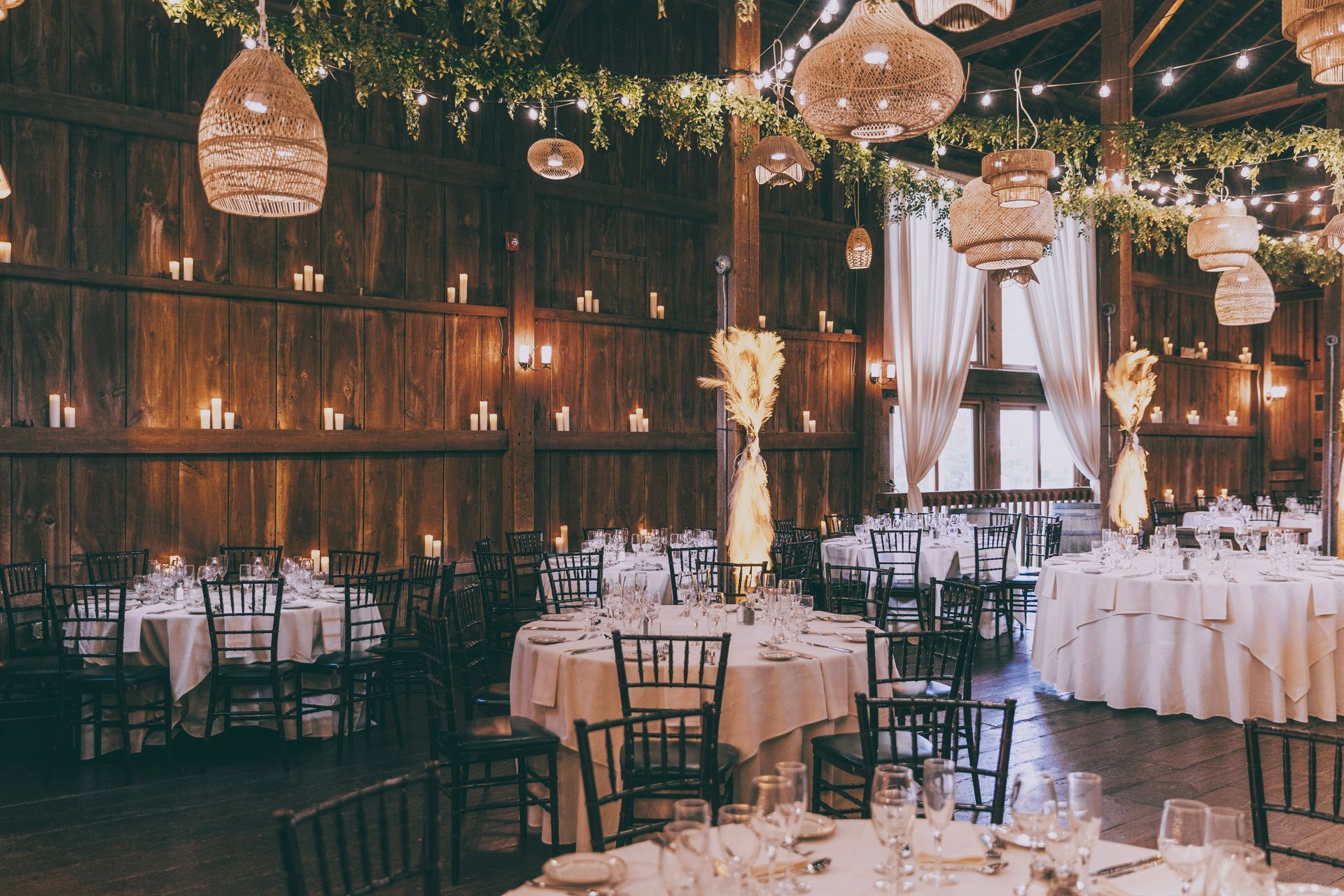 Rustic barn wedding reception with round tables, warm string lights, and chandeliers