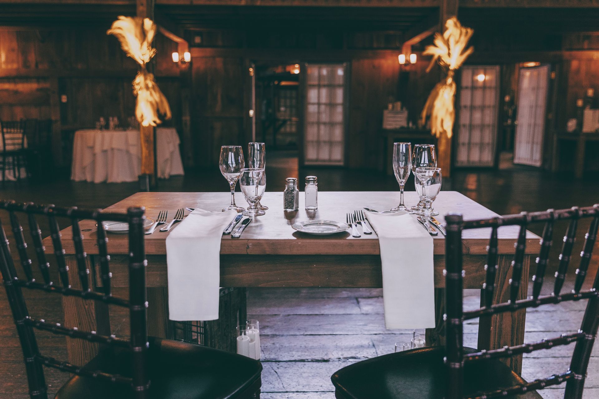 Formal dining table set for two in a dimly lit, elegant banquet hall with tall chairs and candles