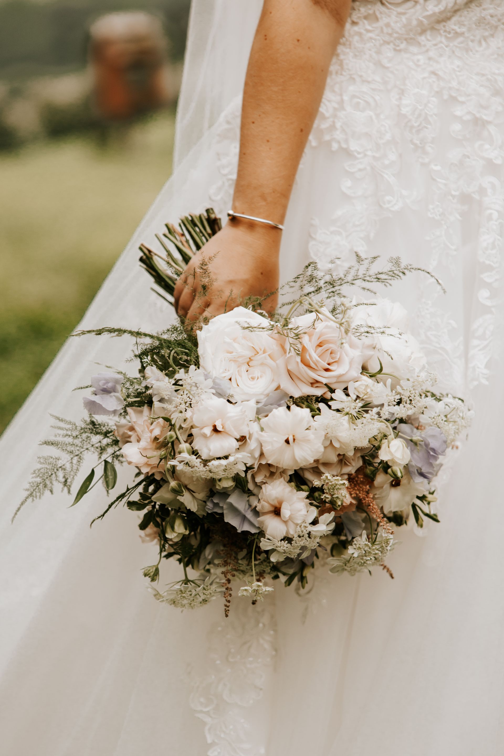 Bride holding a white and green wedding bouquet beside a lace wedding dress
