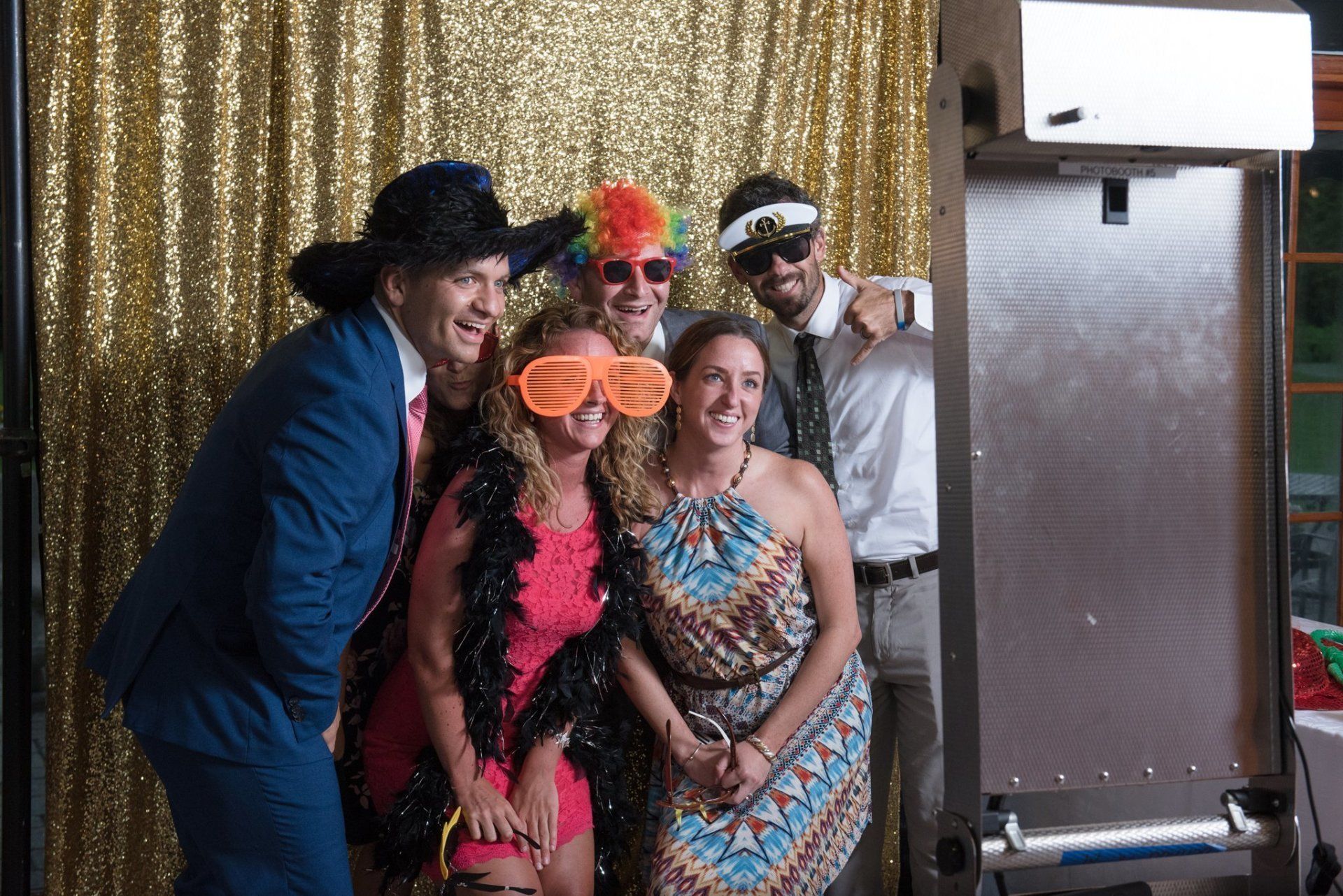 Four people posing in colorful costumes and sunglasses at a photo booth with a gold backdrop