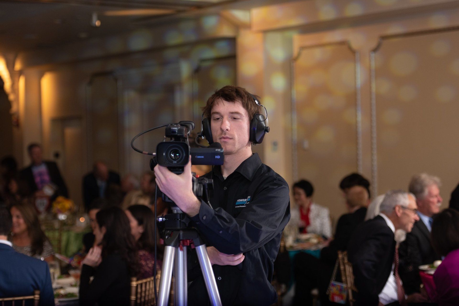 Videographer filming with a camera on a tripod at a crowded indoor event