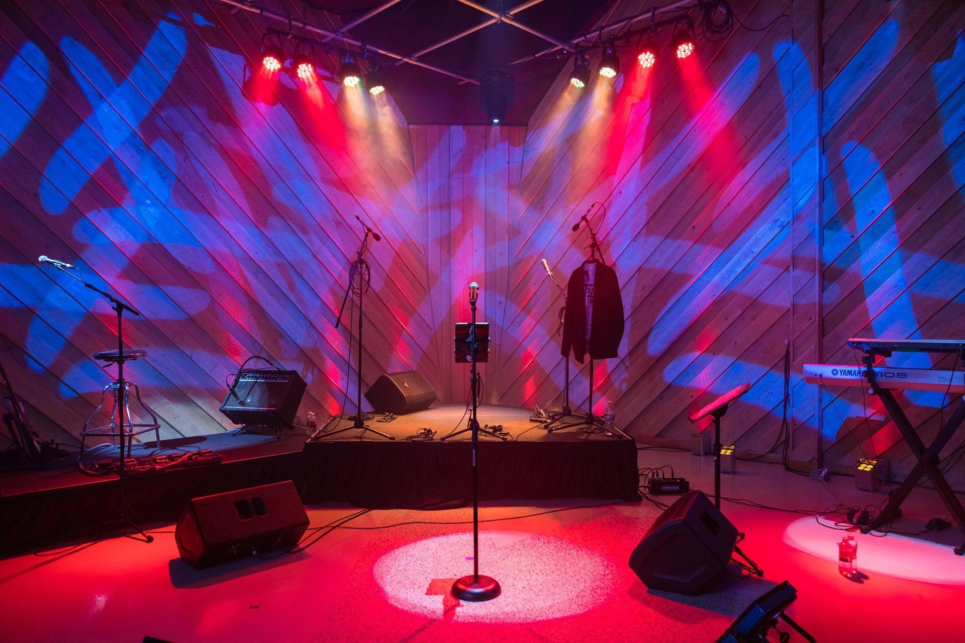 Empty concert stage with microphones, instruments, and red-blue lighting effects