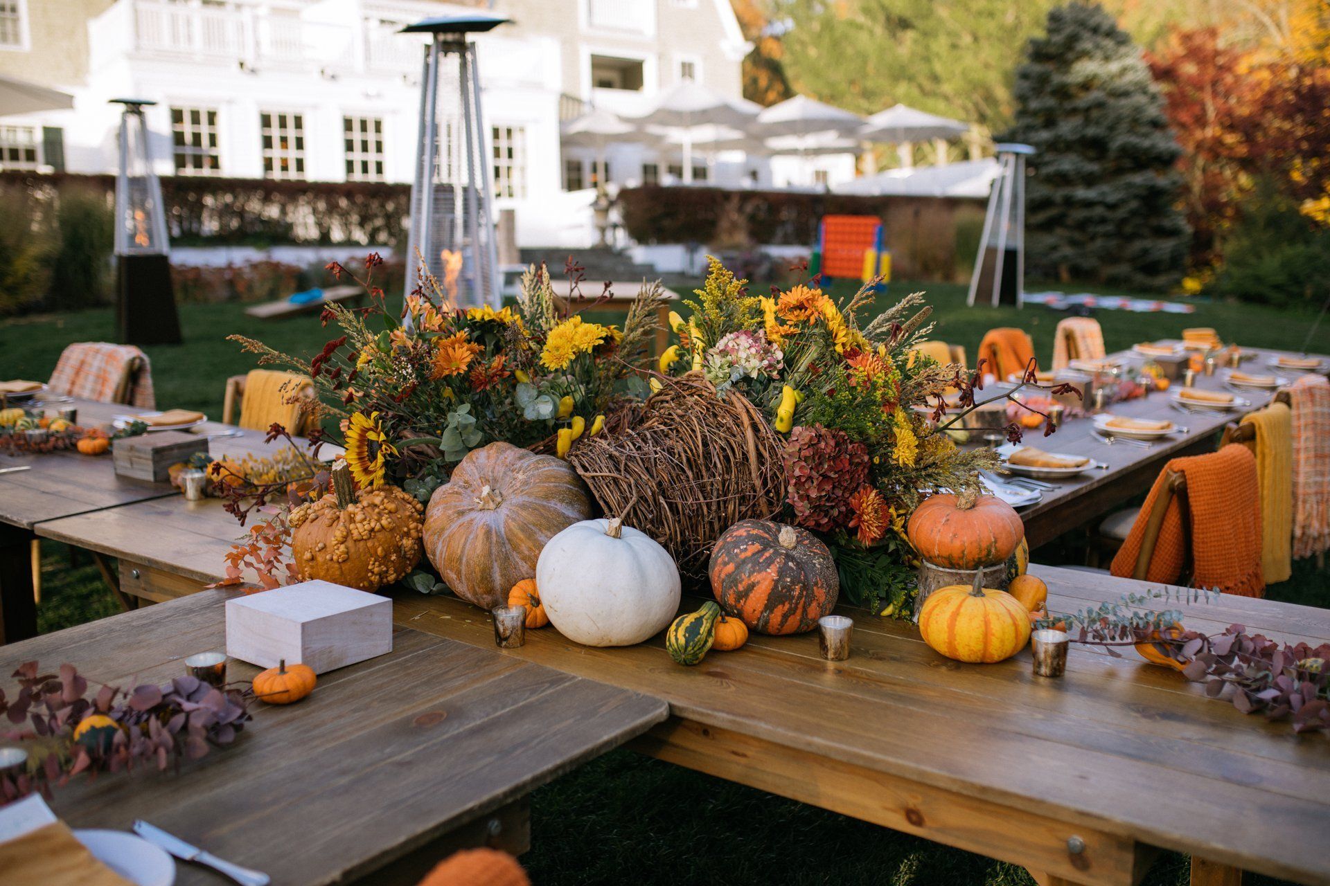 Autumn harvest tablescape with pumpkins, gourds, flowers, and candles on a rustic outdoor dining table