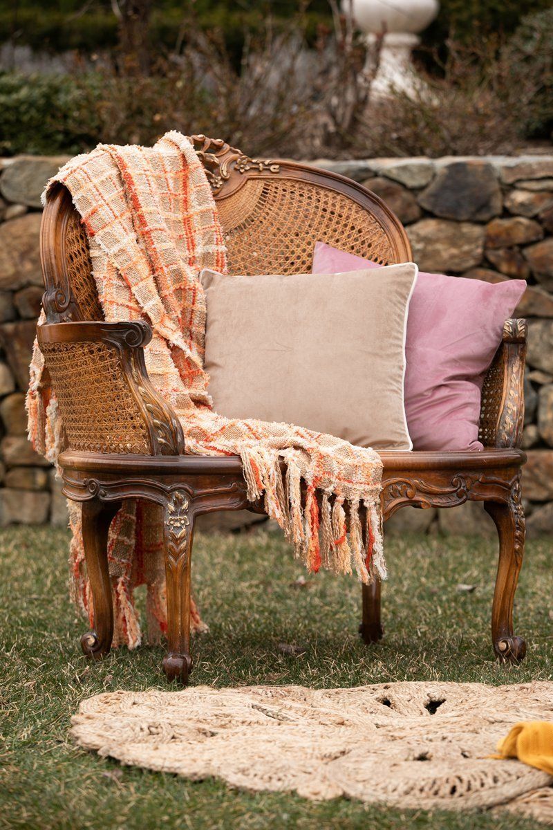 Rustic wicker chair with a blush pillow and striped throw blanket in a garden setting