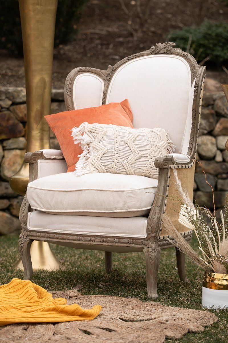White upholstered outdoor armchair with orange and cream pillows on a rustic patio