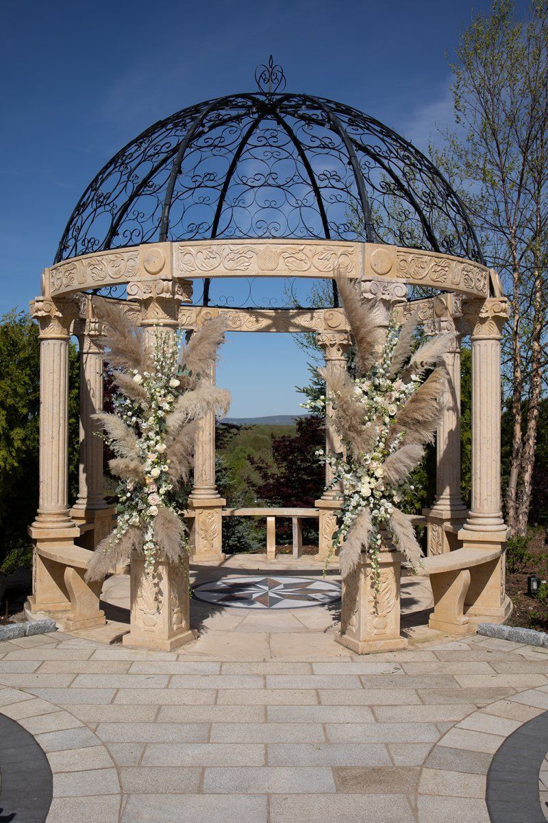 Stone gazebo with floral garlands and a black domed roof on a sunny patio