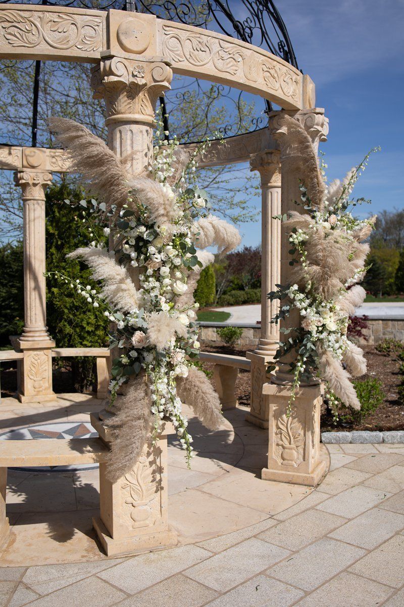 Floral arrangements draped over a stone gazebo in a sunny outdoor wedding setting