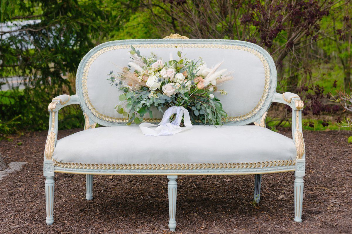 White vintage loveseat with floral cushion and bouquet in a garden setting
