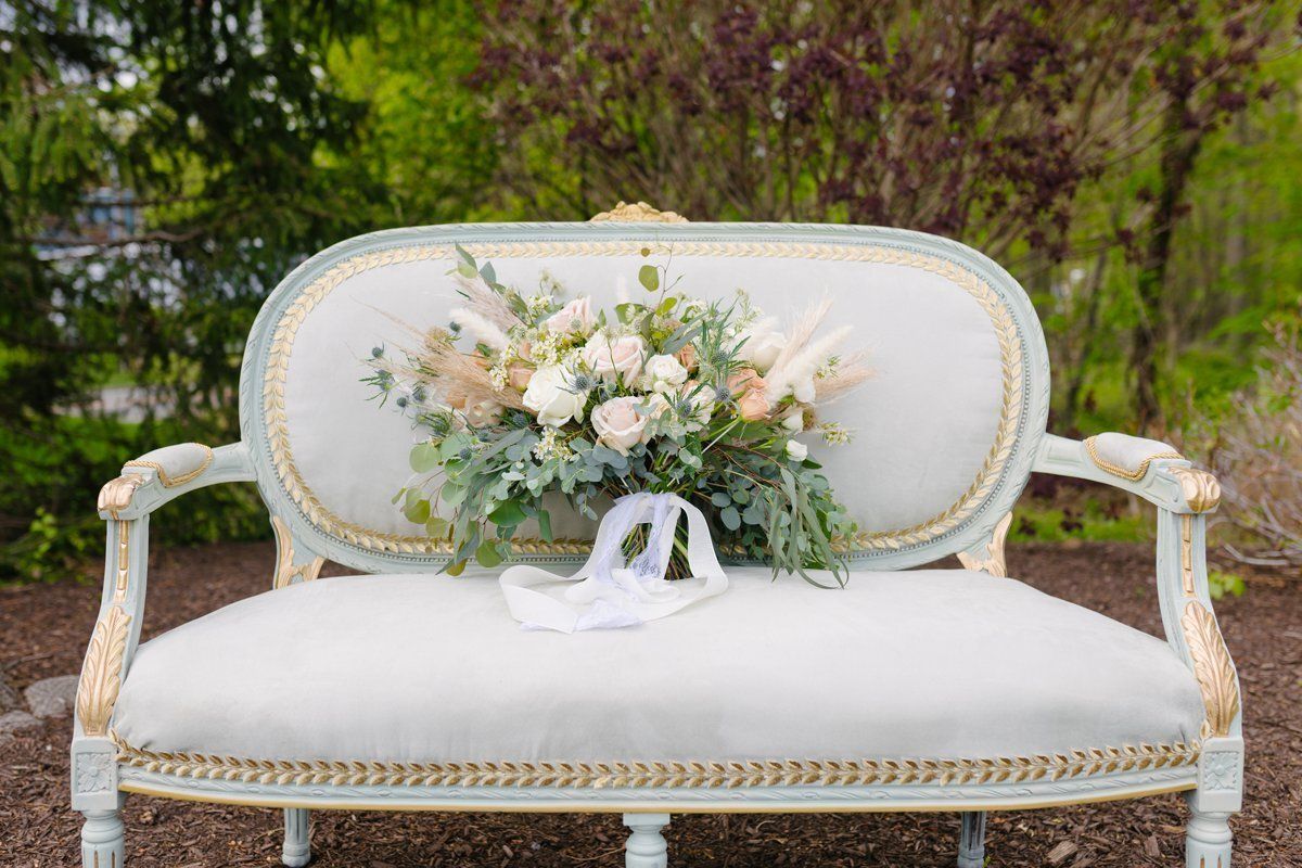 White vintage loveseat with pastel floral arrangement outdoors in a garden