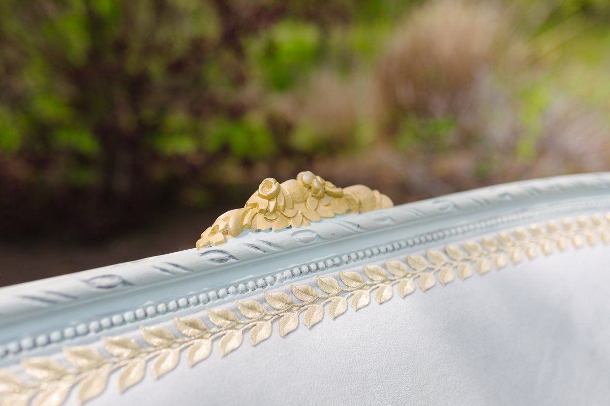 Close-up of a white upholstered chair with gold trim and ornate tufted detail