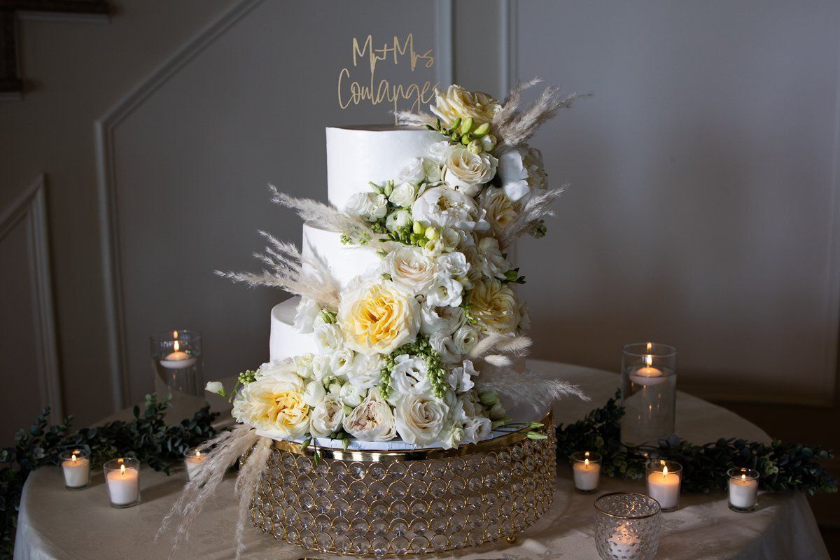 White floral wedding cake on a decorated table with candles and greenery cords