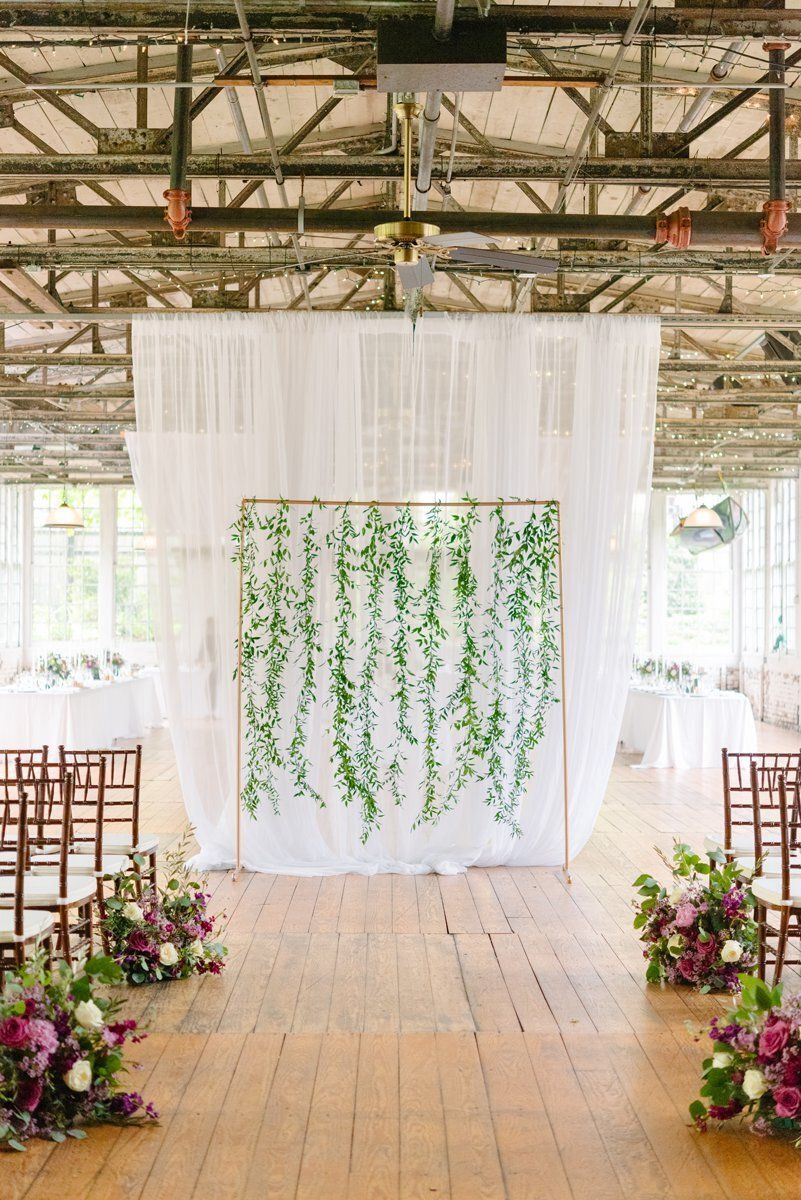 Decorated wedding aisle with white drapes, hanging greenery, and floral arrangements in an open pavilion