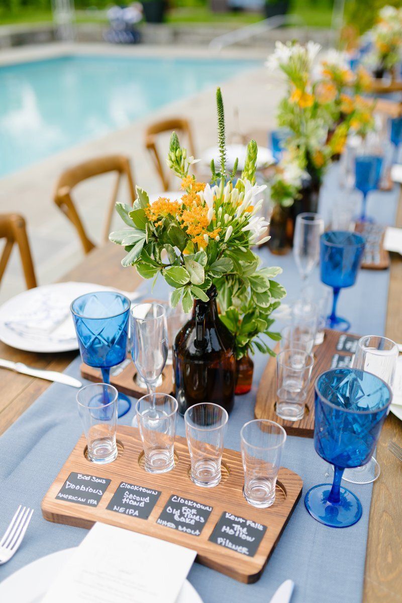 Poolside table set with blue goblets, flowers, and glasses on a wooden tray