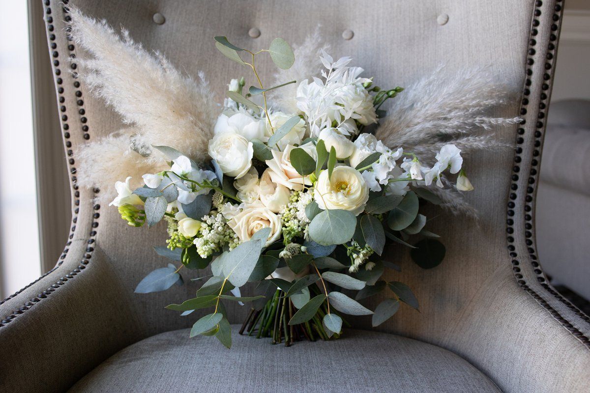White floral bouquet with greenery and pampas grass on a beige upholstered chair