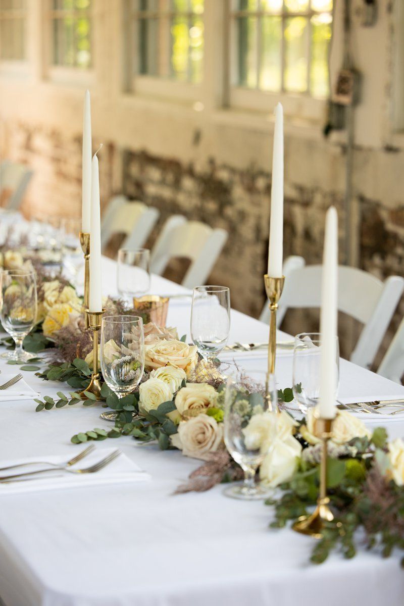 Elegant outdoor dining table with white linens, candles, and white floral arrangements