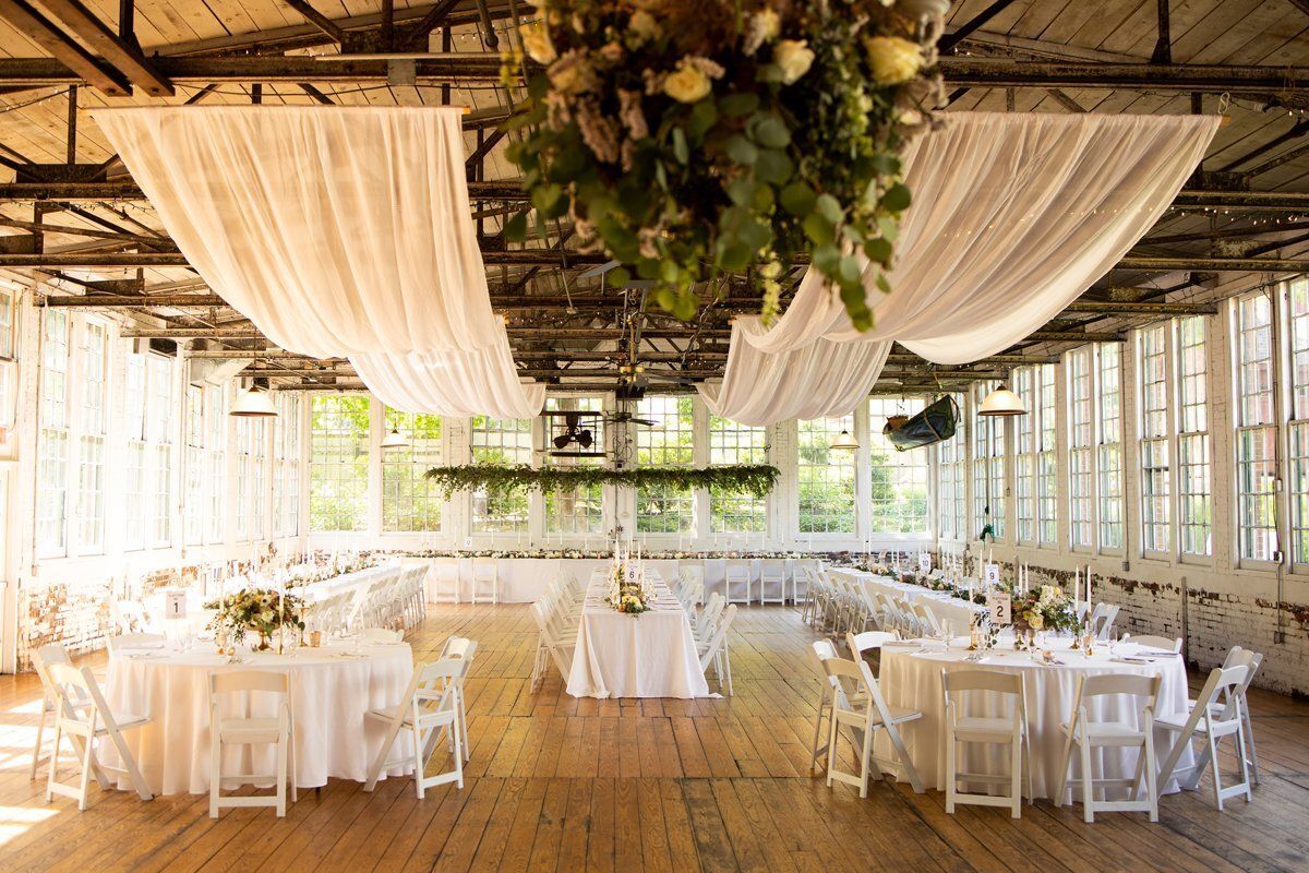 Elegant wedding reception hall with white-draped tables, hanging greenery, and warm wooden floors