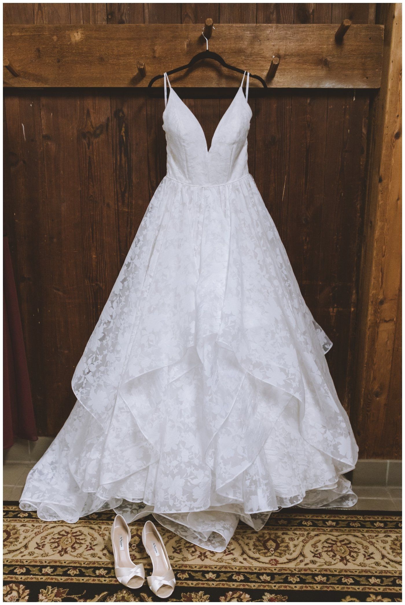 White wedding dress hanging on a wooden door, with lace details and shoes beneath it