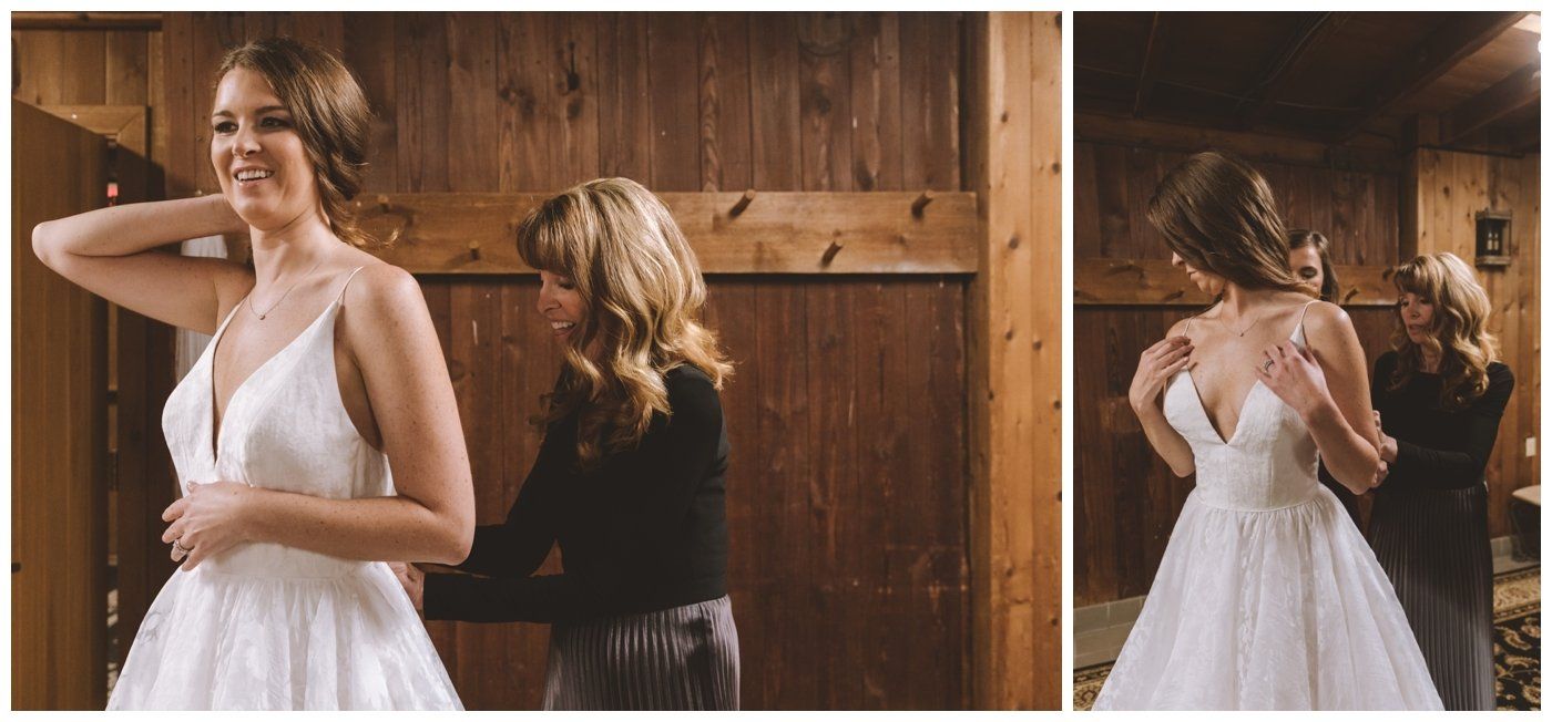 Bride in a white dress smiling while another woman adjusts the back of her gown in a wooden room