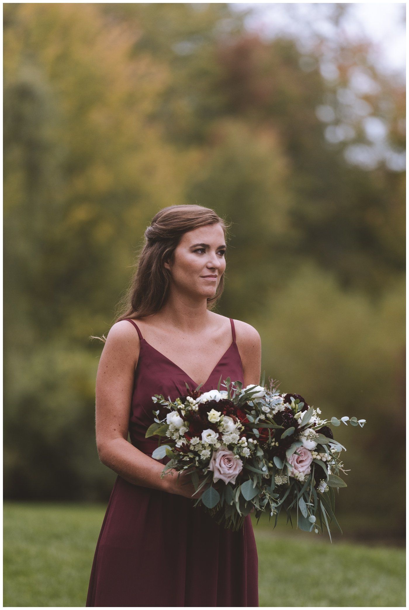 Woman in a burgundy dress holding a bouquet in a blurred outdoor garden setting