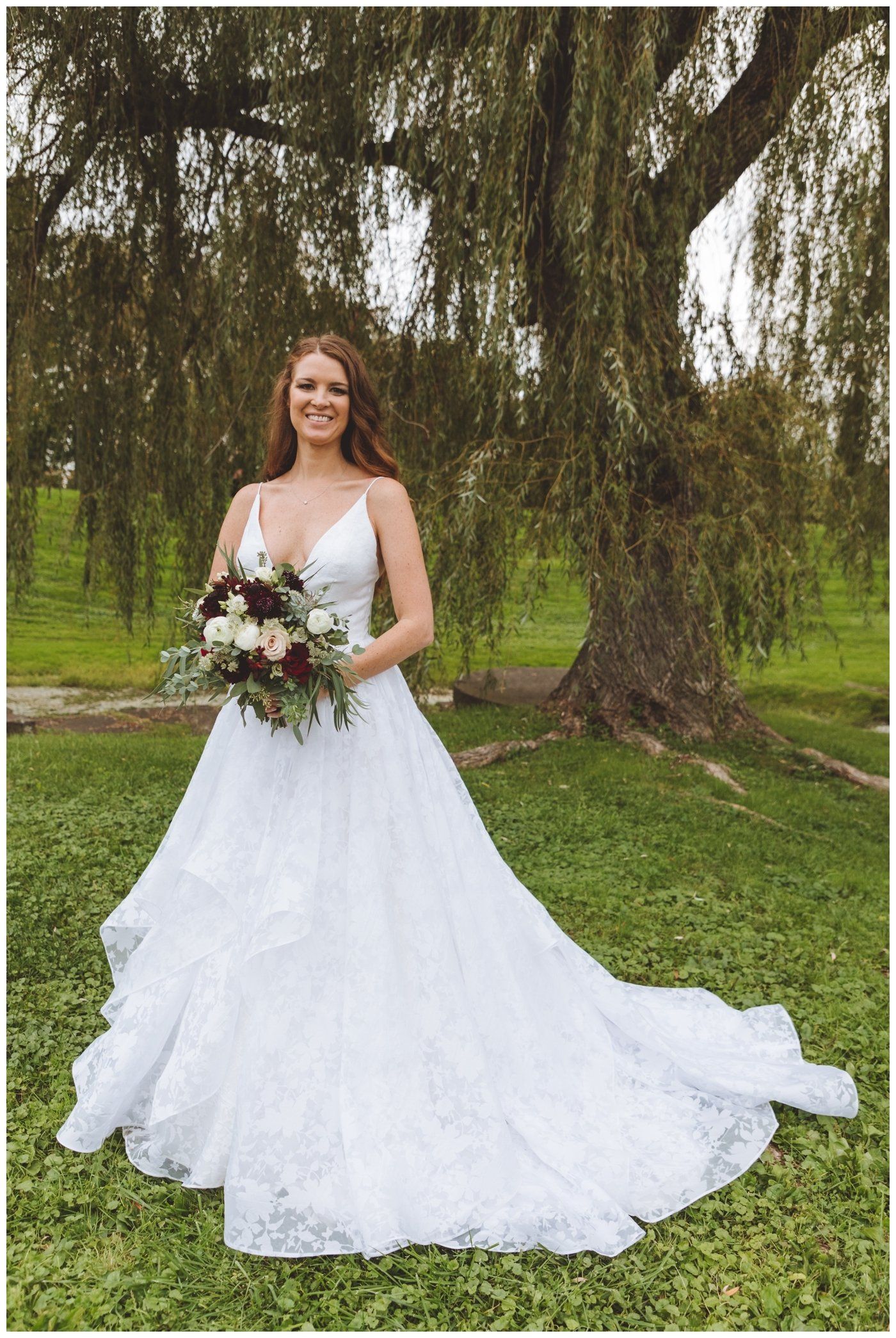Bride in a white wedding dress holding a bouquet in a grassy park beneath trees