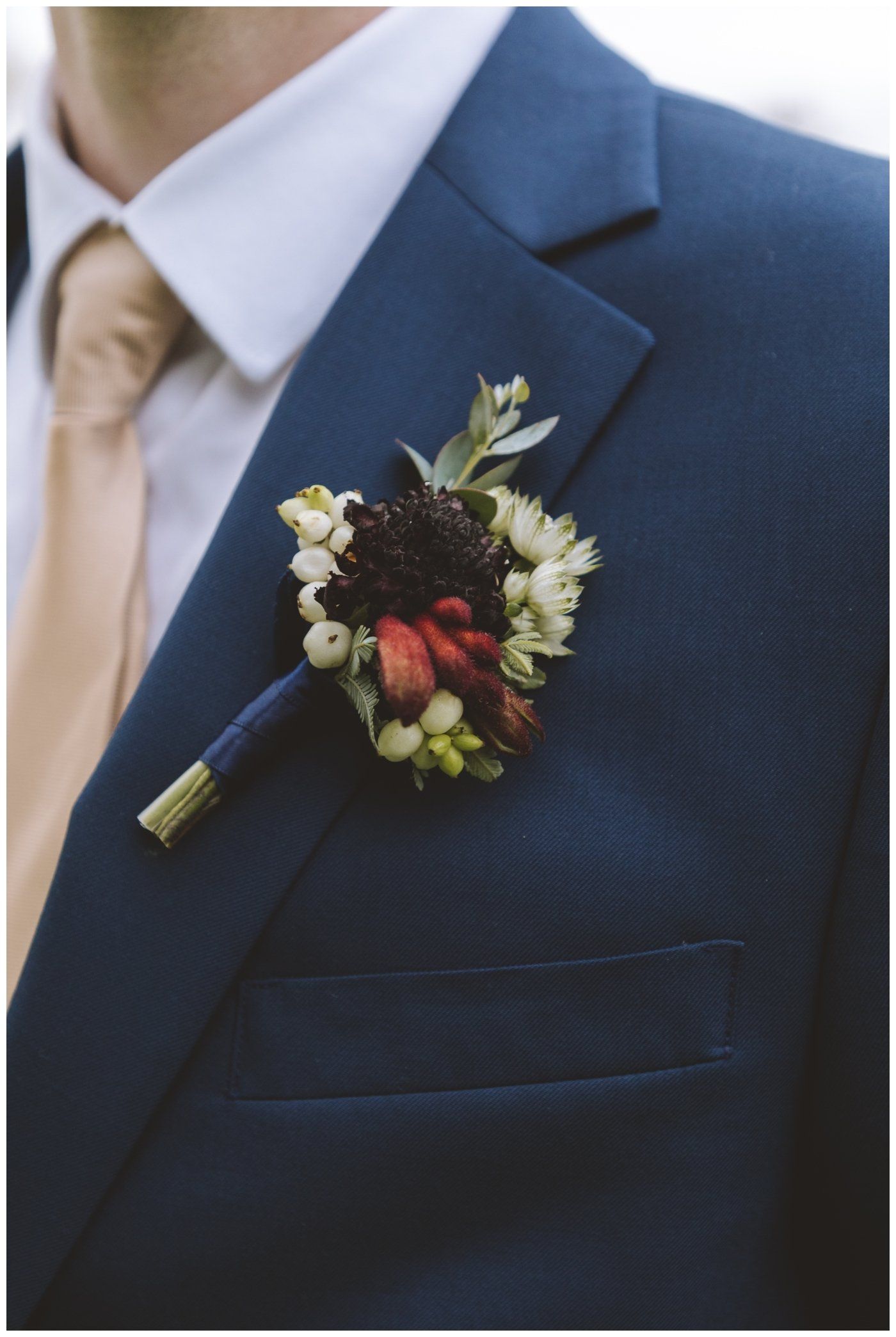 Navy suit jacket with cream tie and floral boutonniere on the lapel