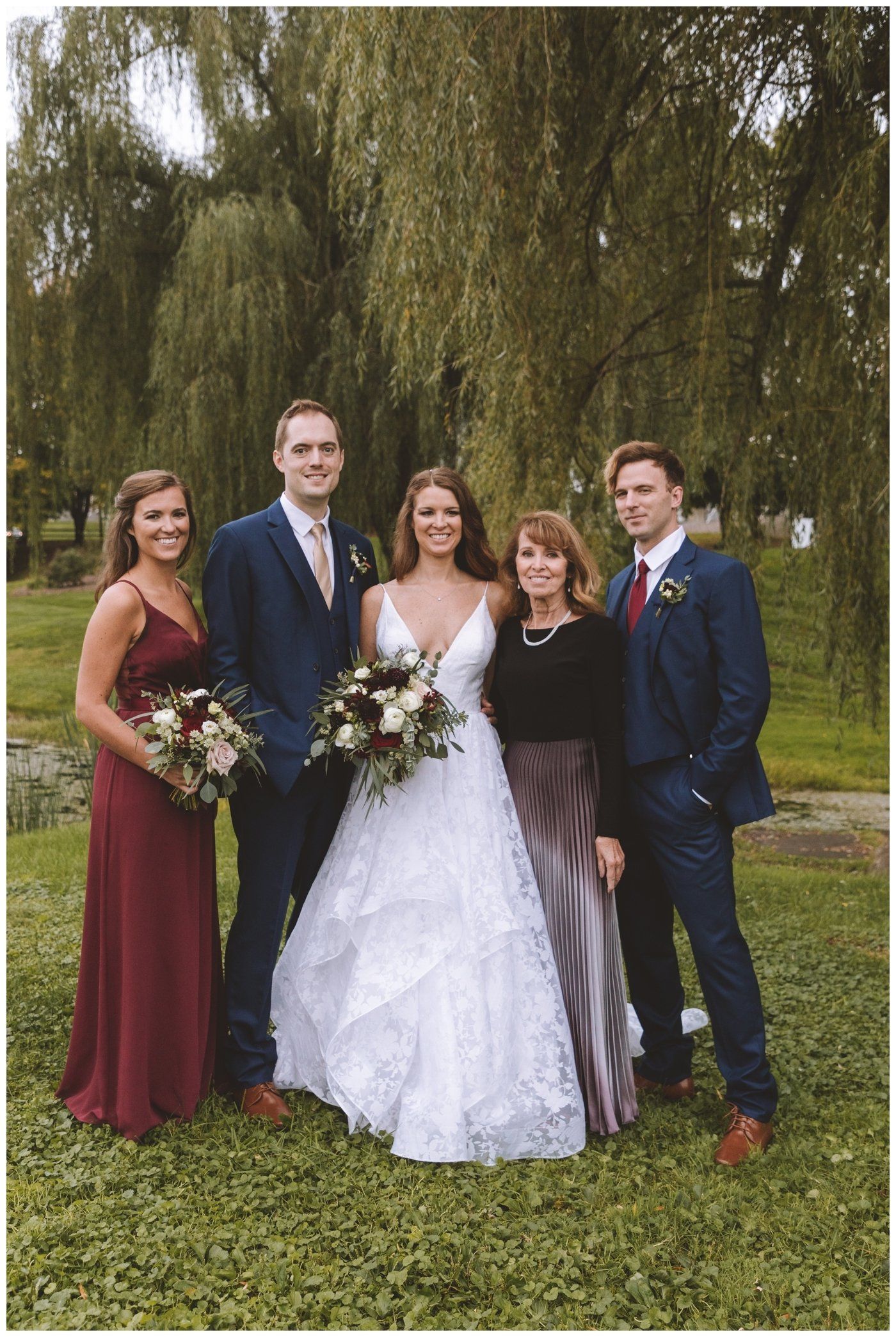Five people dressed for a wedding pose outdoors in front of a willow tree.