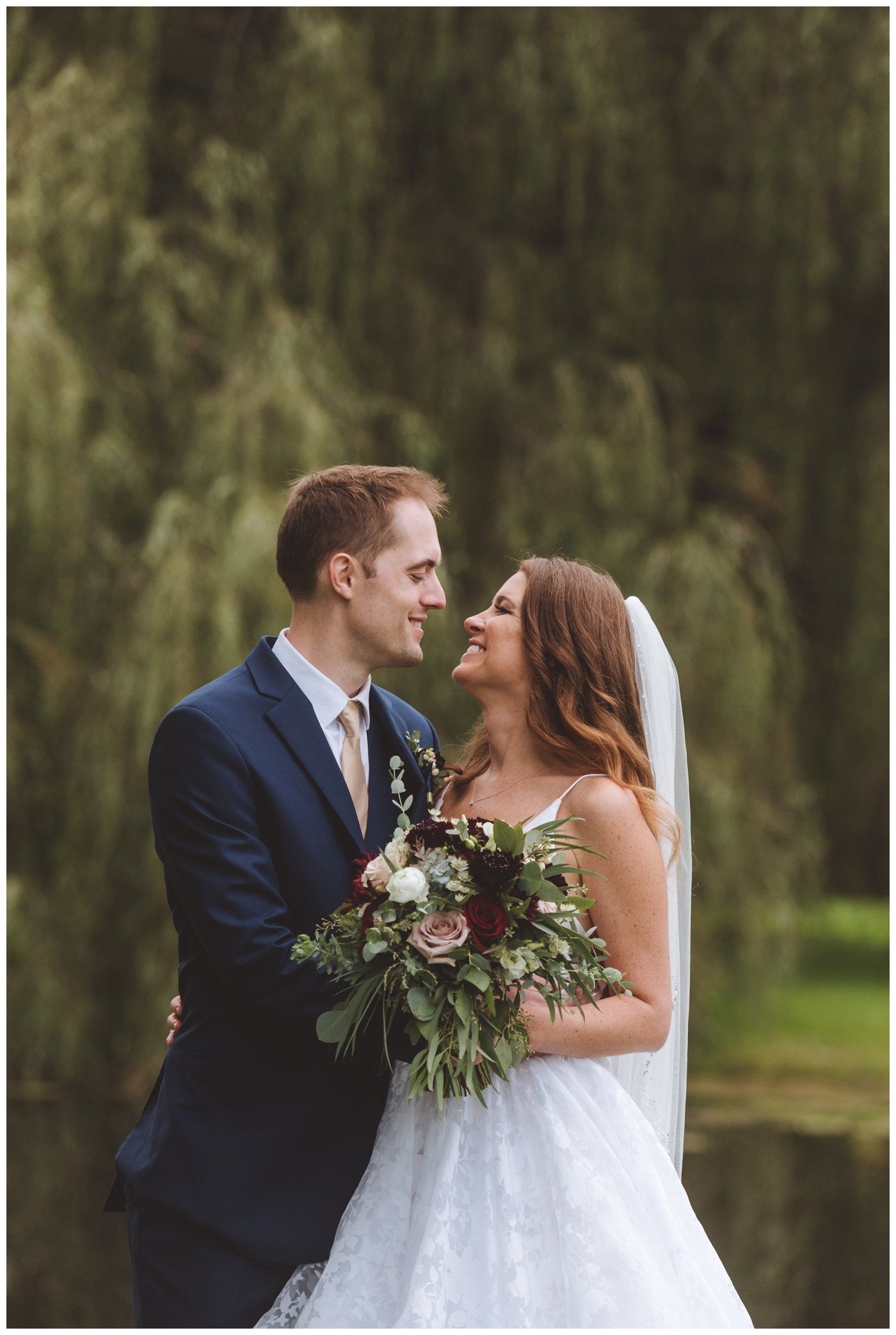 Bride and groom smiling in a garden, holding a bouquet and standing close together