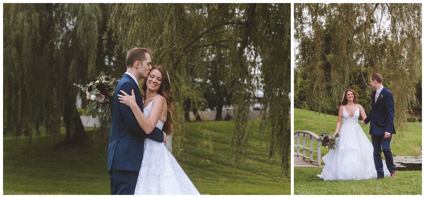 Bride and groom pose in a grassy park under a willow tree, with the bride in a white gown and the groom in a dark suit.