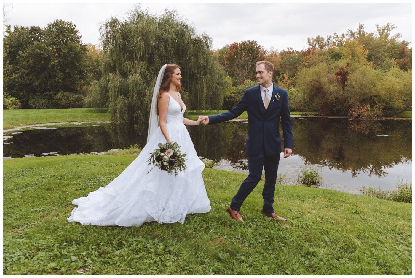 Bride and groom holding hands on a grassy lawn beside a pond and trees