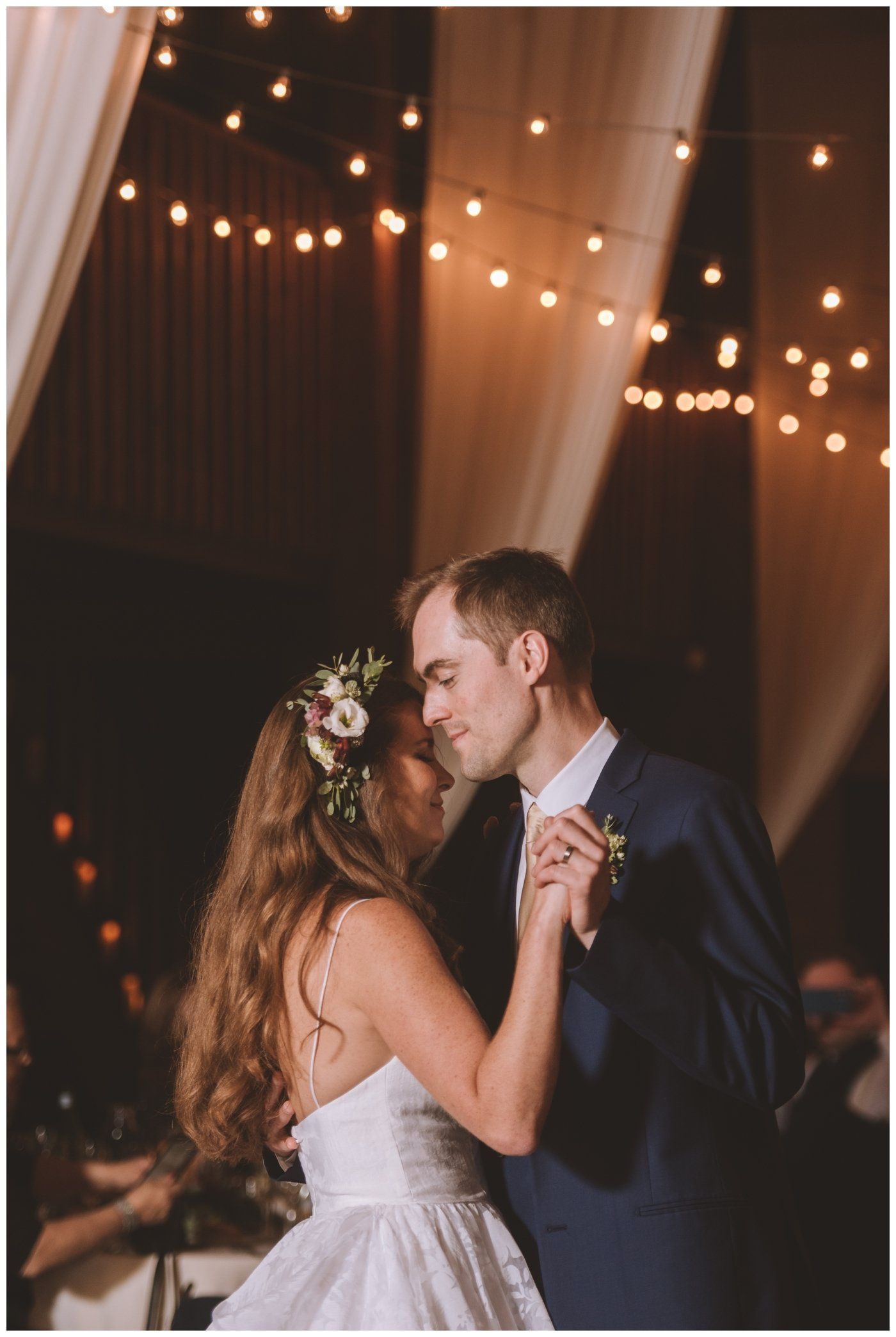 Bride and groom slow dancing under warm string lights at a wedding reception